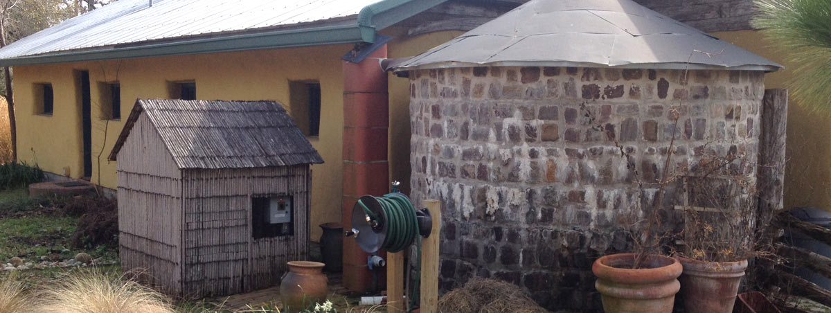 A stone rainwater tank outside of a house. 
